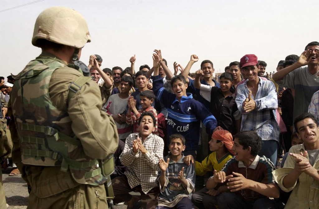 A U.S. Marine is greeted with wild cheers by a crowd of Iraqi men and boys.