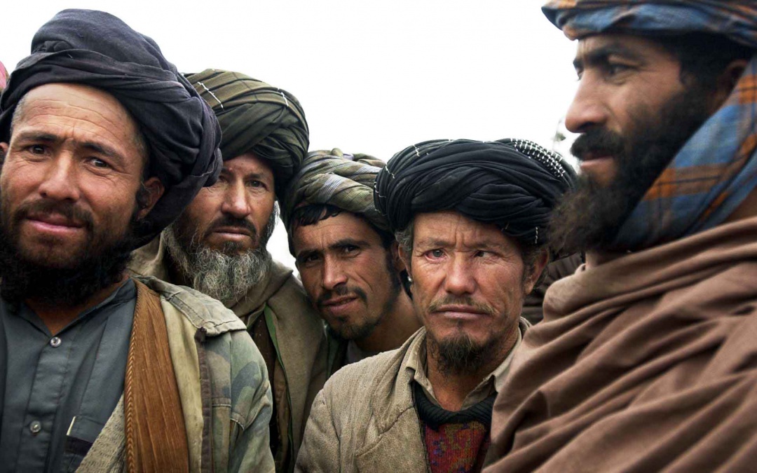 Afghan men surround and stare at a photographer and her camera.
