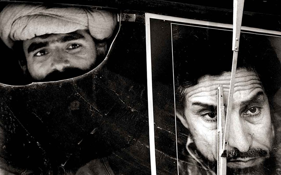 A Taliban soldier peers out of a broken windshield with a poster of Ahmed Shah Masood, a symbol of his surrender, during the Afghanistan War.