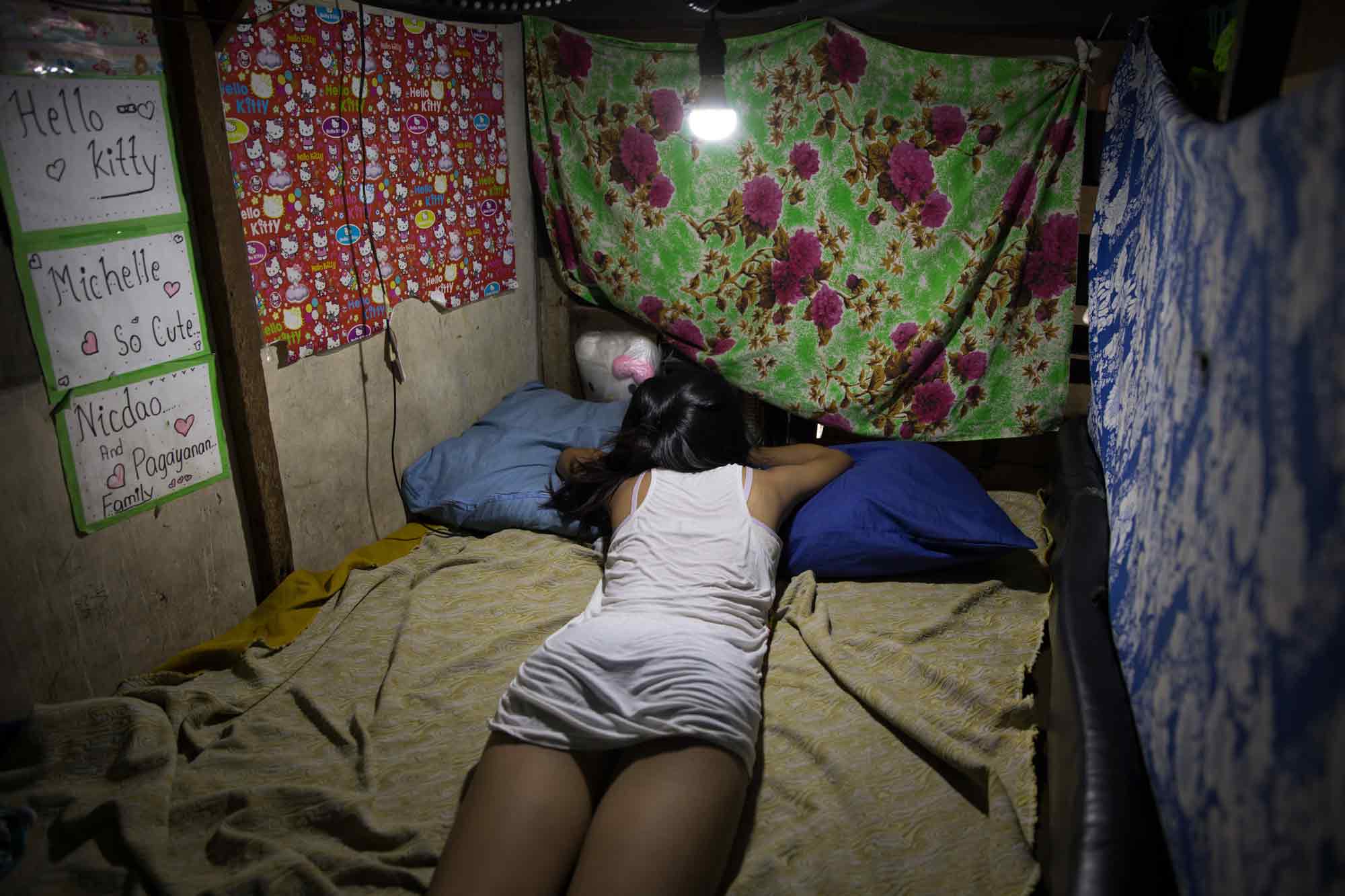 Michelle Nicdao, 14, rests in the privacy of her makeshift sleeping quarters in their rooftop unit, where she lives with her mother and three brothers at the Tenement in Taguig, Philippines. Michelle's great grandfather was an original awardee of a unit at the Tenement and her grandparents also reside on the property. Her father was on a path to becoming a professional basketball player but drugs killed his career, said her mother Maria Oliva Nicdao.