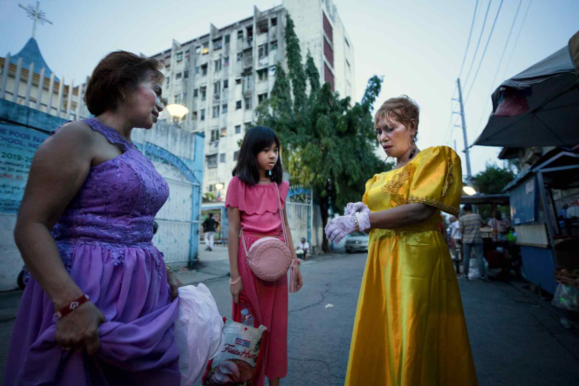 Wearing finery in celebration of Flores de Mayo Mass at Our Lady of the Poor Parish, Heyde Desuasido, Jamilla Padua and Rose Blanca, left to right, depart the church, located in the shadow of the Tenement in Taguig, Philippines.