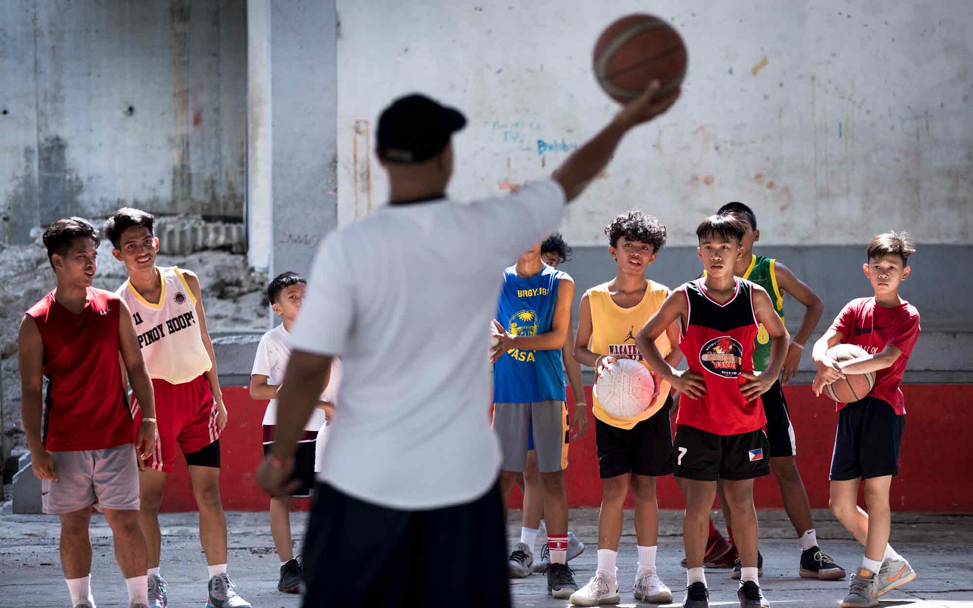 Coach Eddie Barbuena works with impoverished teen boys and girls, offering free basketball training to keep them out of trouble at the Tenement in Taguig, Philippines. Arvie Talorong, Tony Lolos, Alexis Nicdao, Vicver Calungsod, Emman Kyle Atip, and Yuan Taruc, left to right, listen intently to Barbuena, who is a local hero in the community.