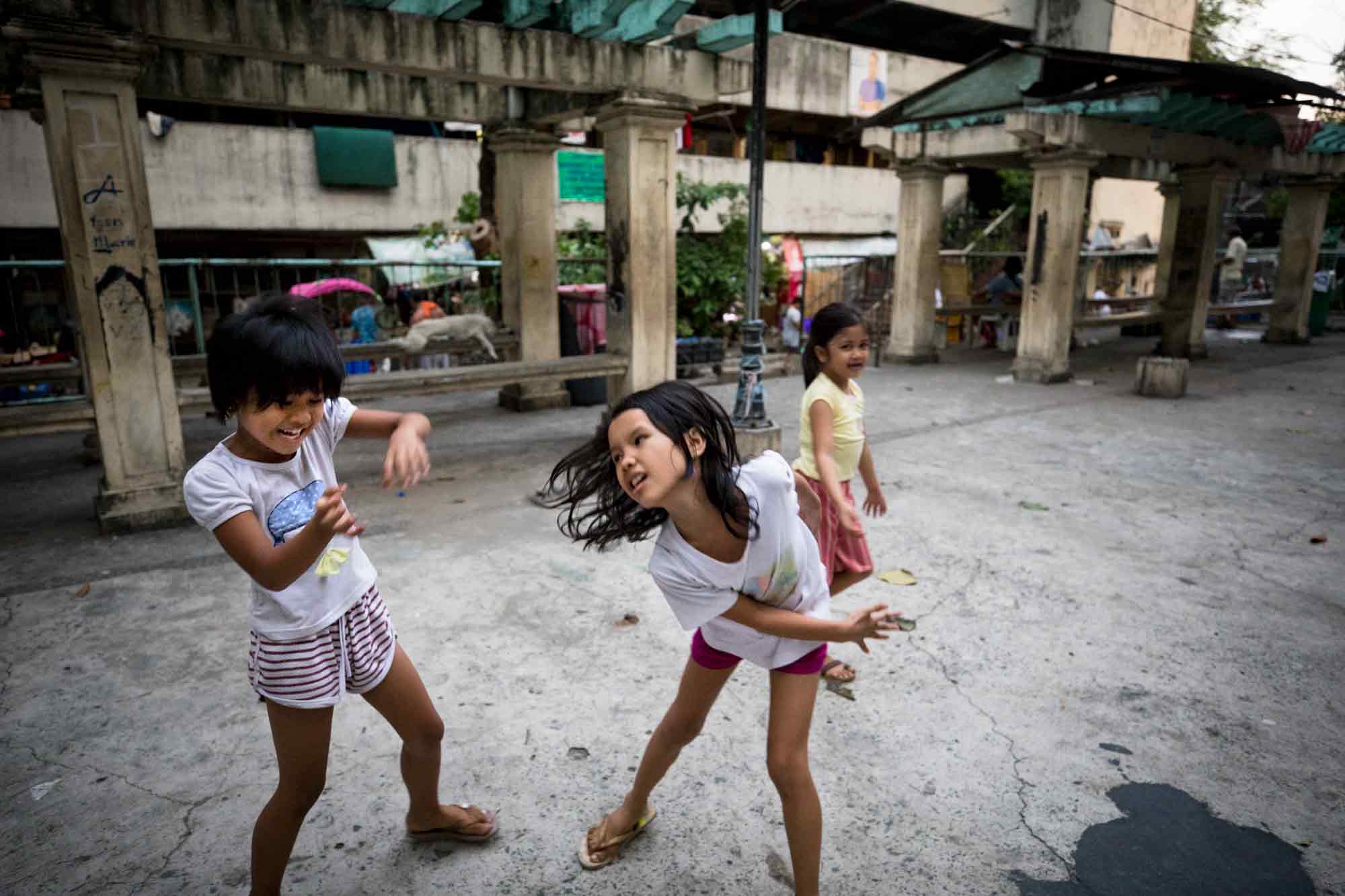 Ayannah Barra and Eona del Rosario, both ages 8, left and right, sometimes fight and other times play in the public space while Joana Sheerin, 7, watches at the Tenement in Taguig, Philippines.