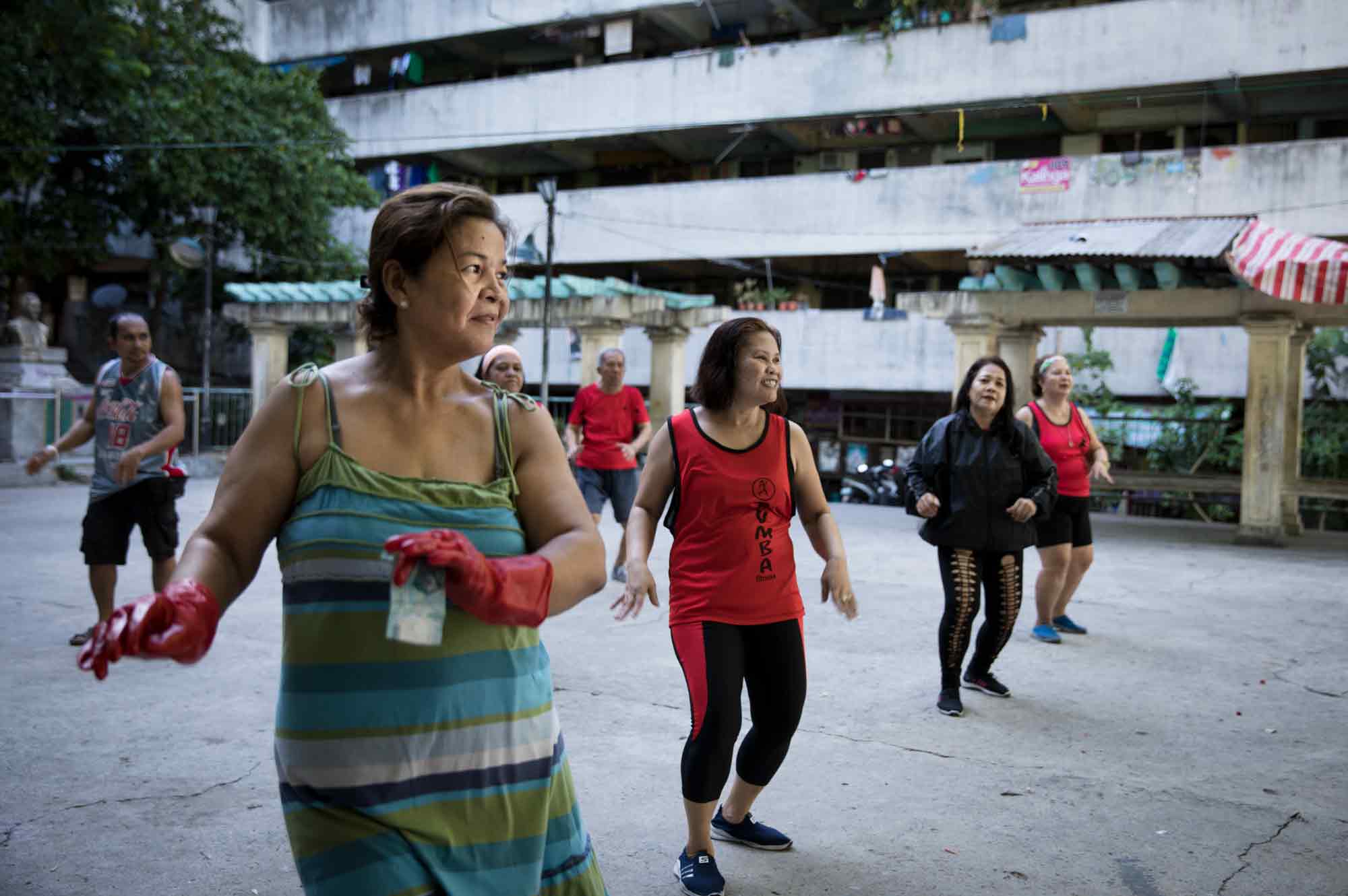 "I'm an addict, so even though I'm busy I can't stop myself from joining them," said Jocelyn Enriquez, far left, who practiced Zumba with money still clasped in her kitchen gloves. She joined Enrique Lukban, Analiza Carullo, Molly Amascual, Rosa Sagaya Donguines, Alice Mistica and Elvira Talorong, rear left to right, in the public square at the Tenement in Taguig, Philippines.